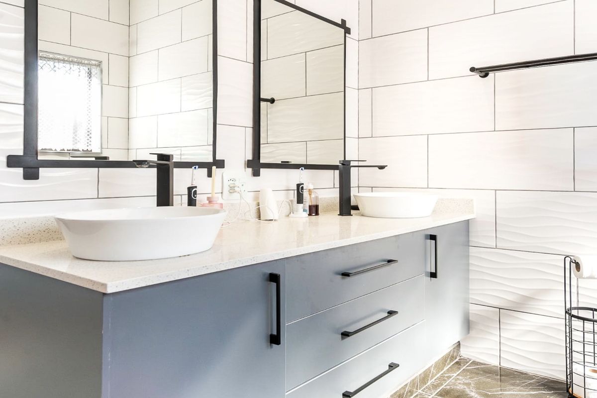 Modern bathroom featuring a double vanity with vessel sinks, matte black fixtures, stone countertop, and contemporary textured wall tiling.
