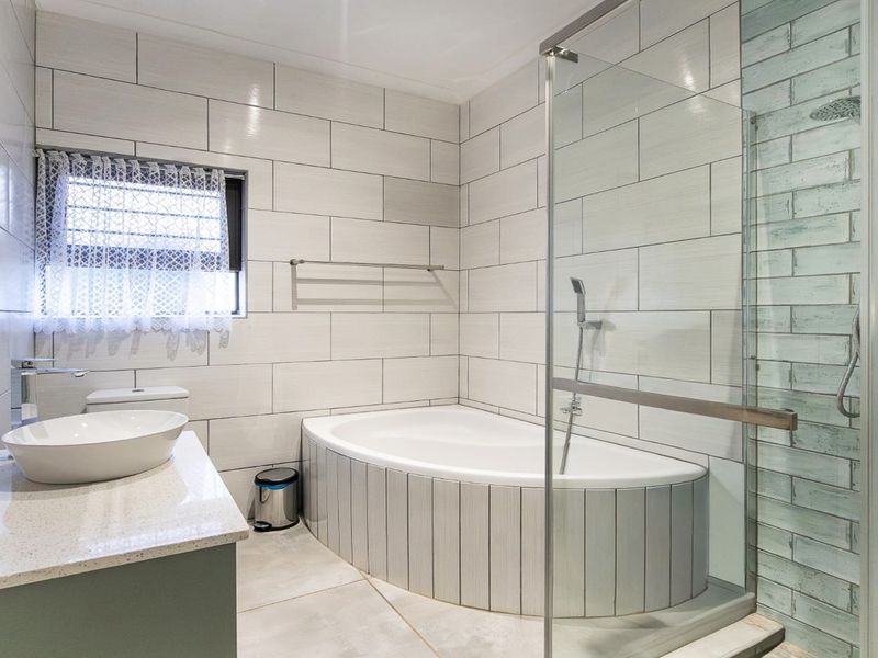 Modern bathroom featuring a vessel sink on a stone vanity, a built-in bathtub, and a separate glass-enclosed shower with contemporary wall tiling.
