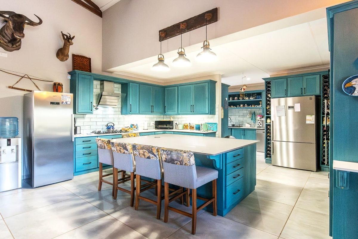 Spacious kitchen featuring vibrant blue cabinetry, a large central island with seating, subway tile backsplash, and modern stainless steel appliances.