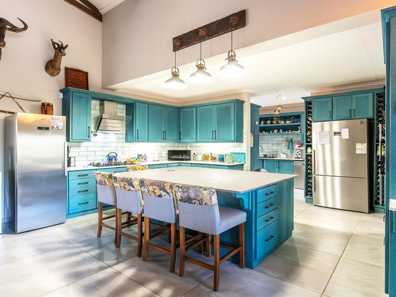 Spacious kitchen featuring vibrant blue cabinetry, a large central island with seating, subway tile backsplash, and modern stainless steel appliances.