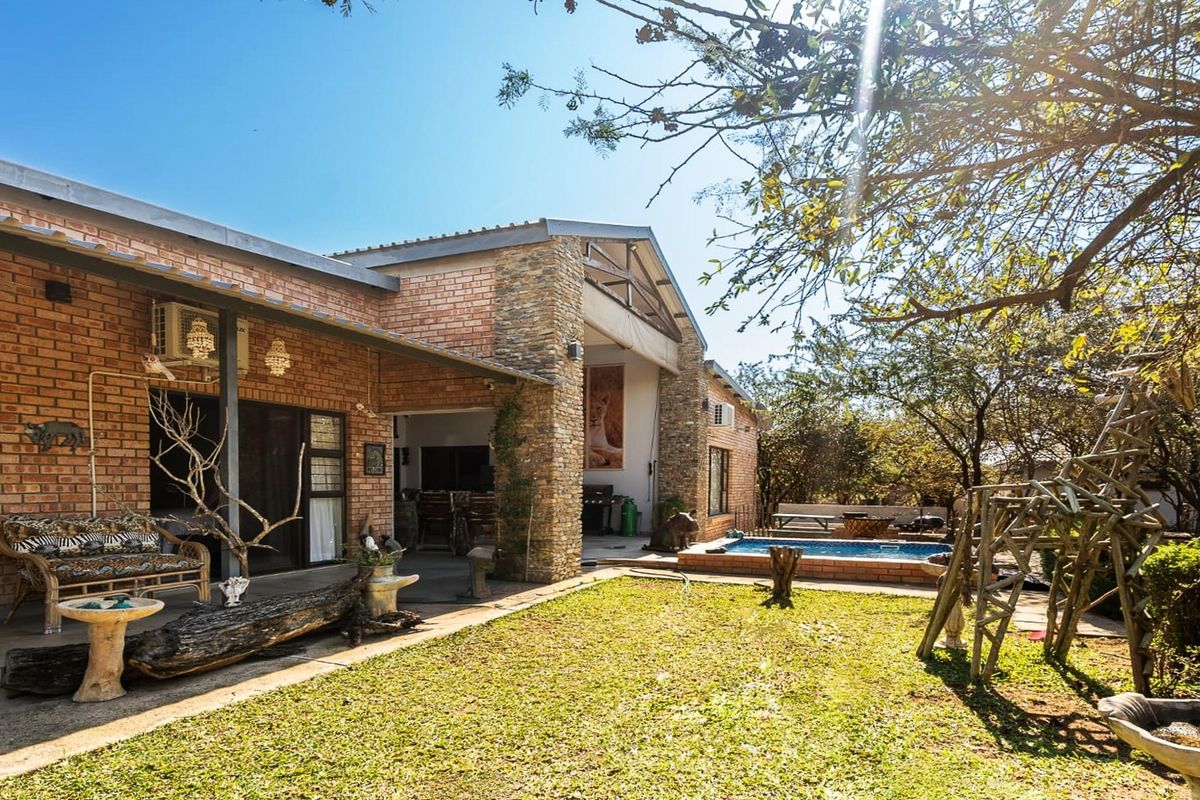 Rear view of the property featuring an exposed brick and stone facade, a covered patio area, and a swimming pool set within a garden.