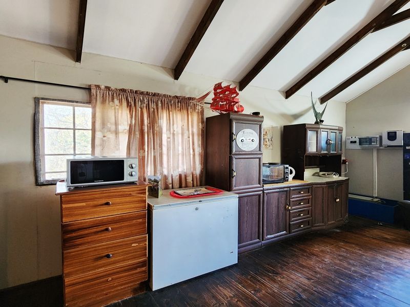 A rustic kitchen area featuring exposed timber ceiling beams, dark wood cabinetry, and timber flooring, offering potential for a modern renovation.