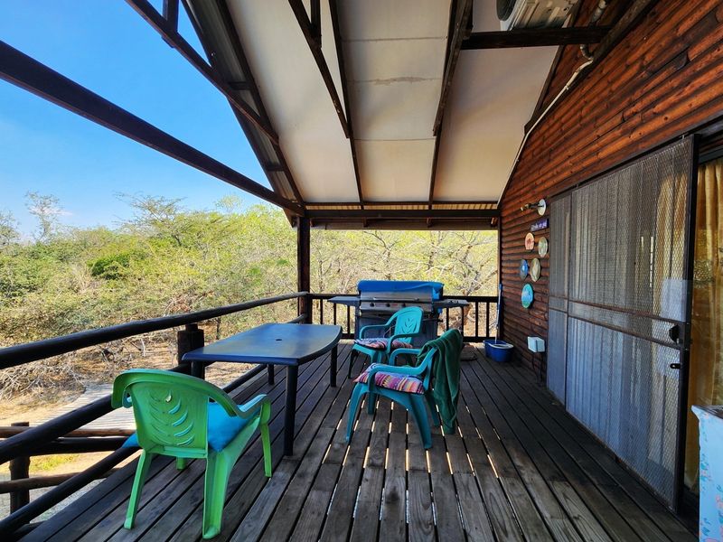 A covered timber deck balcony featuring natural wood finishes and a security screen door, overlooking the surrounding bushveld landscape.