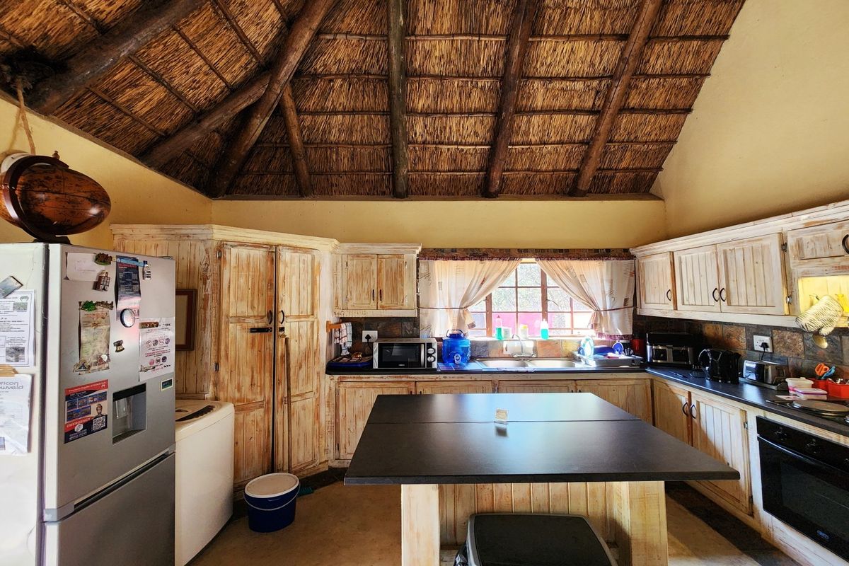 Rustic kitchen featuring a high thatched ceiling with exposed timber beams, wooden cabinetry, stone backsplash, and a central island.