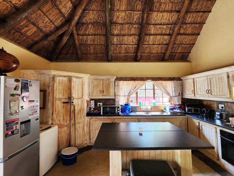 Rustic kitchen featuring a high thatched ceiling with exposed timber beams, wooden cabinetry, stone backsplash, and a central island.