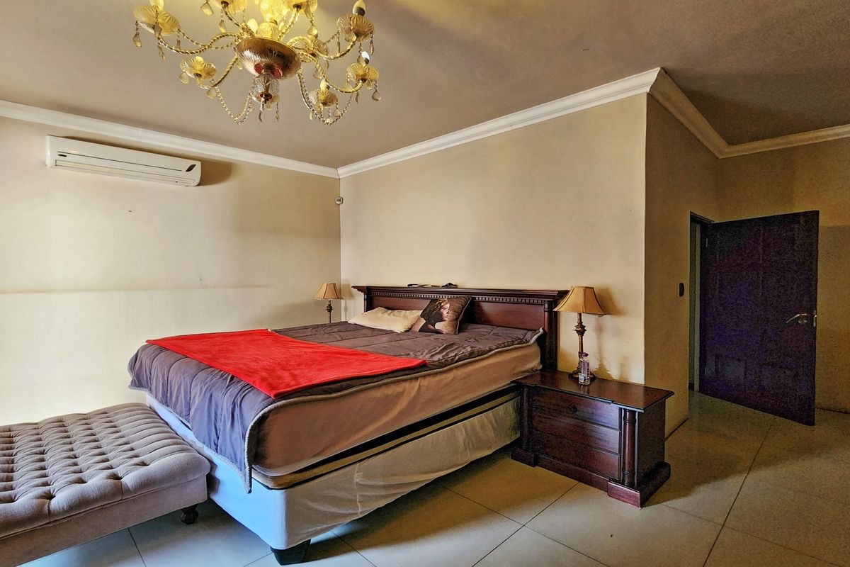 A spacious bedroom featuring tiled flooring, crown molding, and a wall-mounted split-system air conditioner.