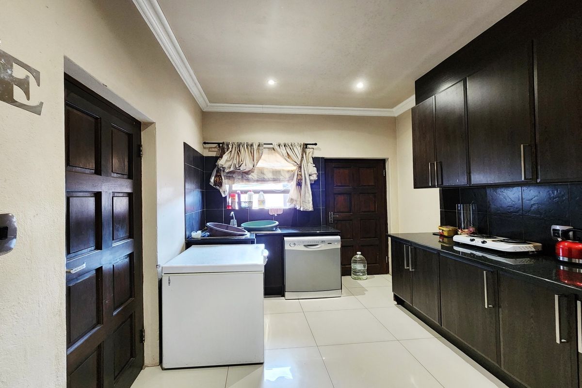 A functional kitchen featuring dark wood cabinetry, granite countertops, black tile backsplash, and tiled flooring with recessed lighting.