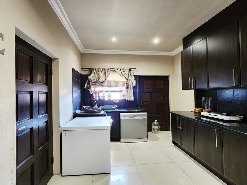 A functional kitchen featuring dark wood cabinetry, granite countertops, black tile backsplash, and tiled flooring with recessed lighting.