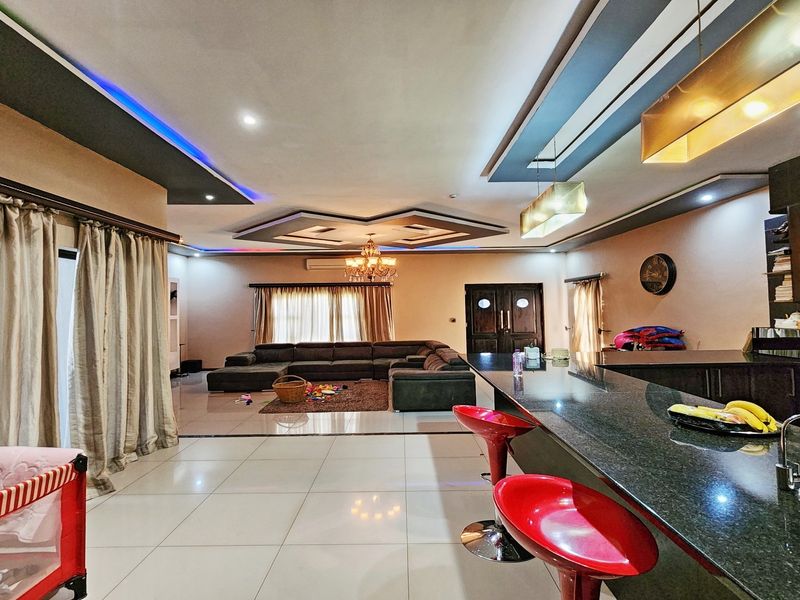 Spacious open-plan living area featuring a modern kitchen with granite island, recessed ceiling lighting, and large tiled floors, creating a seamless flow.