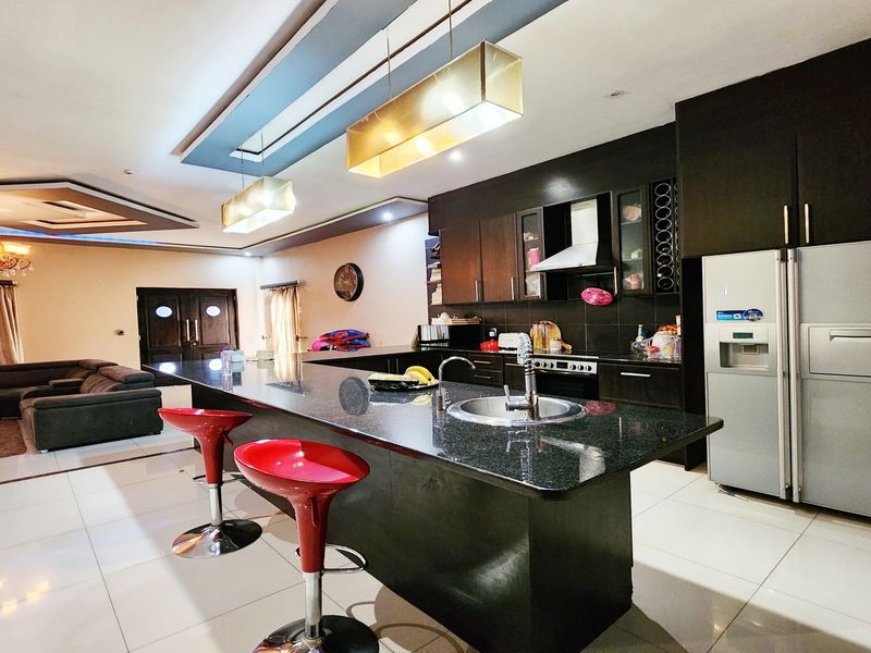Spacious open-plan living area featuring a modern kitchen with a large granite island, dark cabinetry, and integrated lighting, seamlessly flowing into the living space.