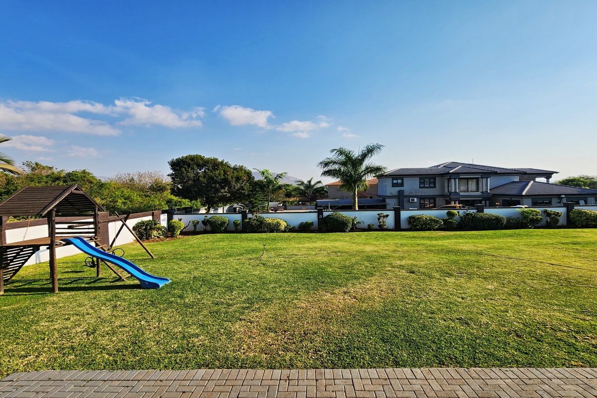 Spacious rear garden featuring a well-maintained lawn, perimeter wall, and paved patio area, offering a clear view of the main residence.