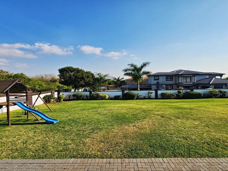Spacious rear garden featuring a well-maintained lawn, perimeter wall, and paved patio area, offering a clear view of the main residence.