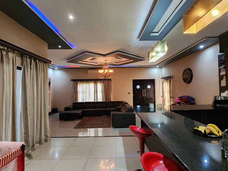 Spacious open-plan living area featuring a modern kitchen with a granite island, recessed ceiling details with ambient lighting, and large format floor tiles.