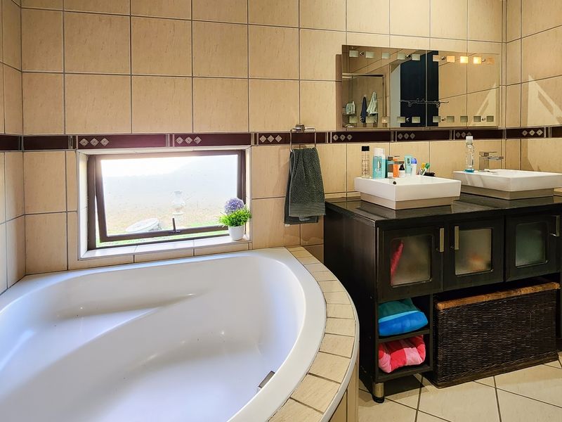 A functional bathroom featuring a built-in corner bathtub, a double vanity with vessel sinks, and neutral wall tiling.