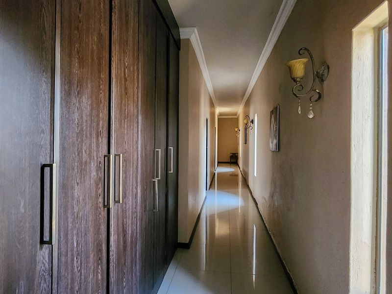 A long, well-lit hallway featuring extensive built-in wooden cupboards, polished tiled flooring, and decorative wall sconces.