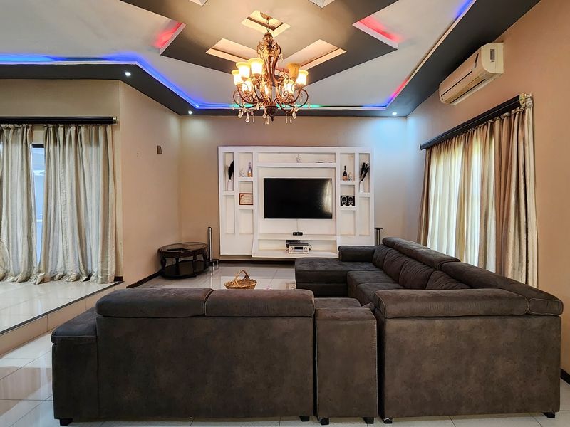 Spacious living room featuring a built-in media wall, decorative recessed ceiling with ambient LED lighting, and a central chandelier.