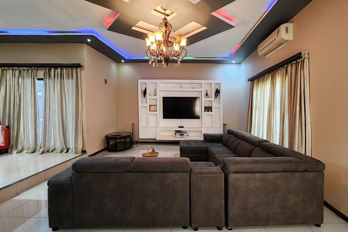 Spacious living room featuring a built-in media wall, decorative recessed ceiling with ambient LED lighting, and a central chandelier.