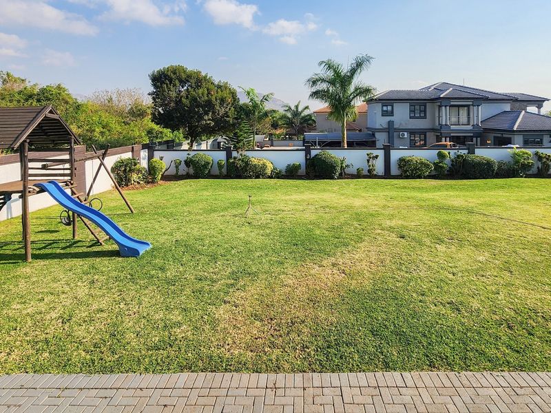 A spacious, well-maintained private garden featuring a large lawn, perimeter wall, and paved patio area, ideal for outdoor recreation.