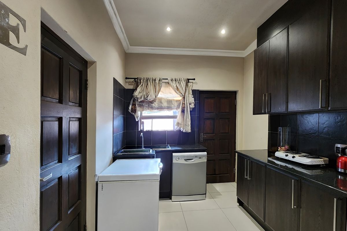 A functional kitchen featuring dark wood cabinetry, granite countertops, black tiled backsplash, and integrated lighting, providing a practical workspace.