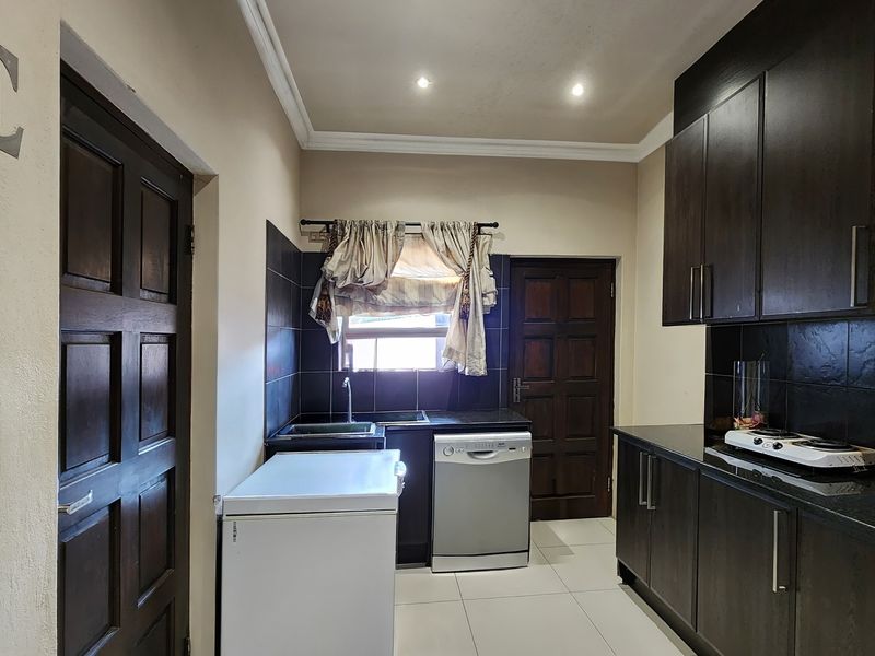 A functional kitchen featuring dark wood cabinetry, granite countertops, black tiled backsplash, and integrated lighting, providing a practical workspace.