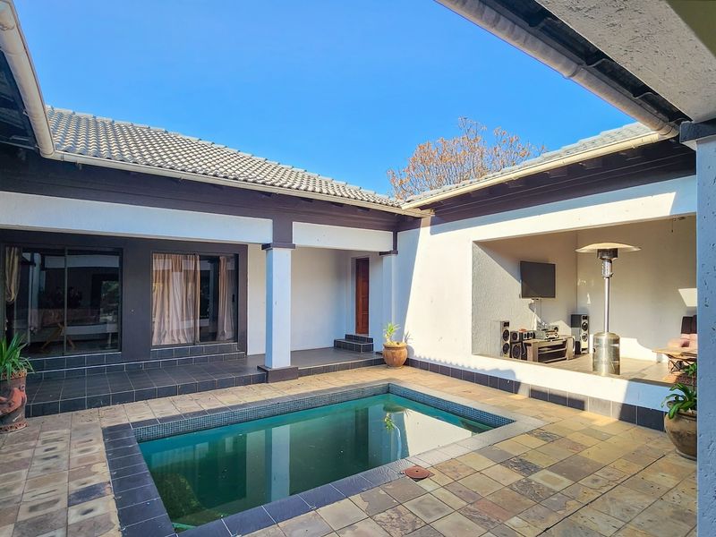 A private courtyard featuring a swimming pool, tiled patio area, and a covered outdoor entertainment space with structural pillars.