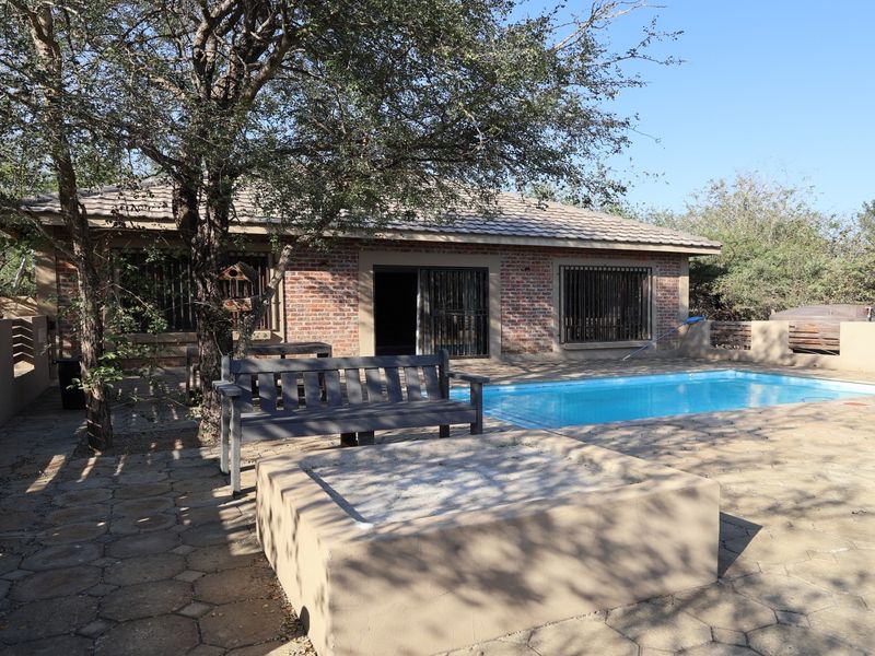 Outdoor pool area featuring a paved patio, built-in fire pit, and a brick-faced house exterior with security bars on the windows.