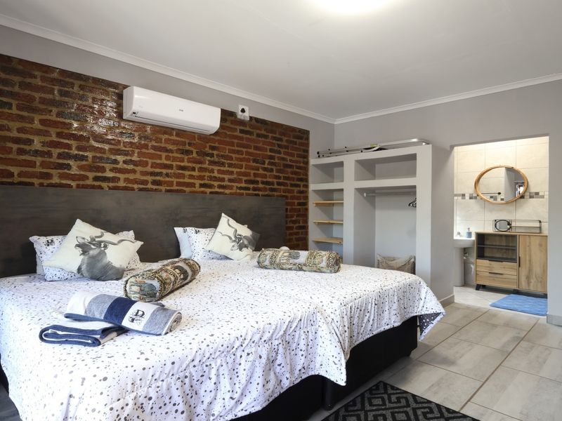Spacious bedroom featuring an exposed brick accent wall, split-system air conditioning, built-in storage shelving, and direct access to an adjoining bathroom.