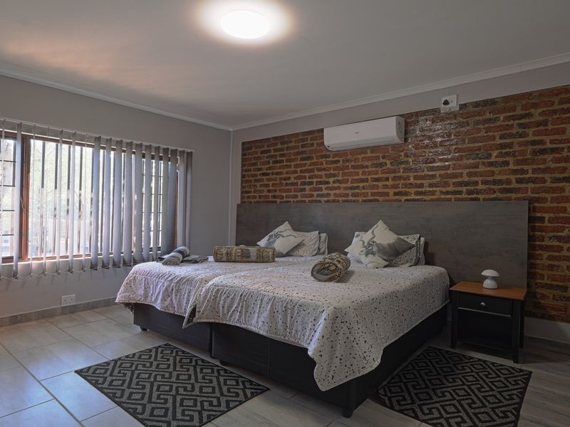 Spacious bedroom featuring an exposed brick accent wall, tiled flooring, and a wall-mounted air conditioning unit.