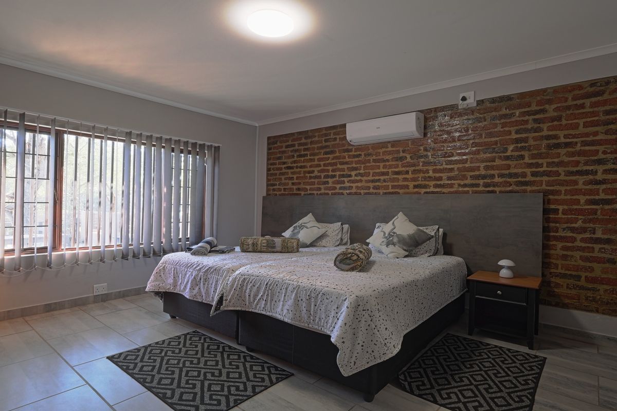 Spacious bedroom featuring an exposed brick accent wall, tiled flooring, and a wall-mounted air conditioning unit.