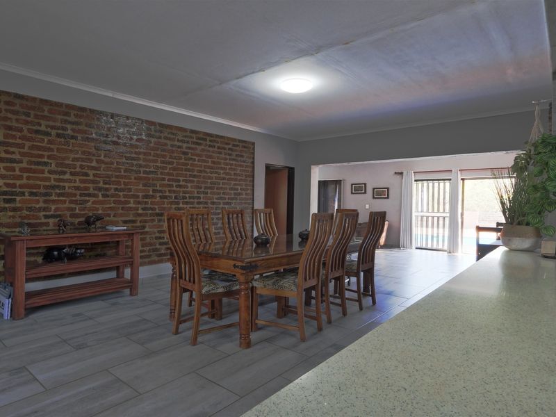 Spacious open-plan living and dining area featuring an exposed brick feature wall, modern tiled flooring, and direct access to the outdoor patio area.
