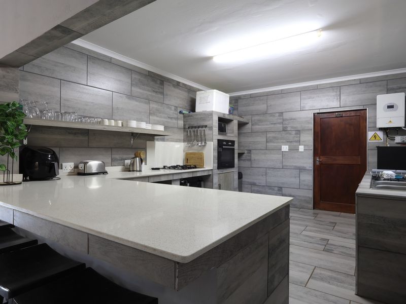 Modern kitchen featuring grey tiled walls, quartz countertops, built-in oven, gas hob, and an integrated inverter system.