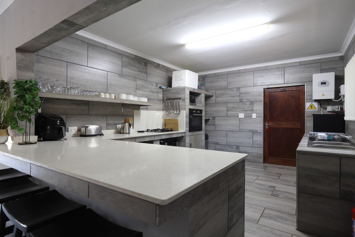 Modern kitchen featuring grey tiled walls, quartz countertops, built-in oven, gas hob, and an integrated inverter system.