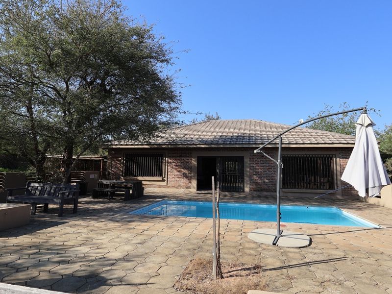 Outdoor pool area featuring a paved patio, brick exterior facade, and a swimming pool set against a natural garden backdrop.