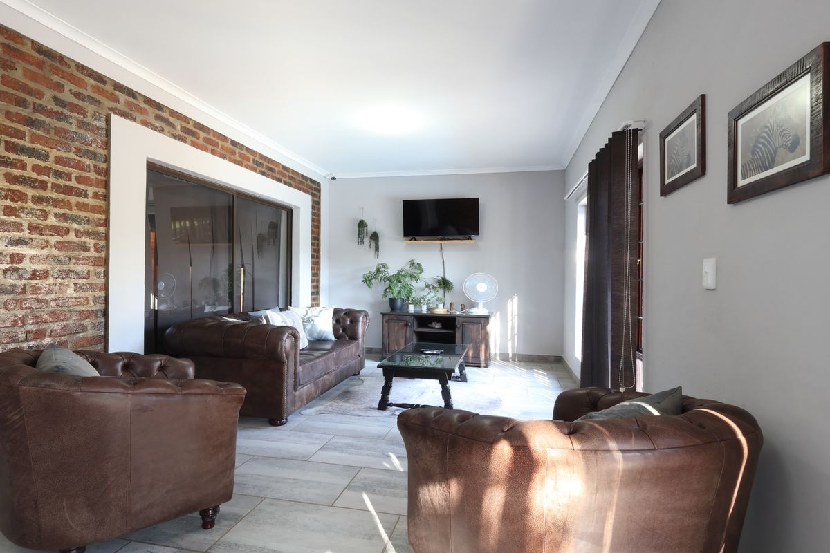 A comfortable living room featuring an exposed brick accent wall, neutral tiled flooring, and large sliding glass doors providing natural light.