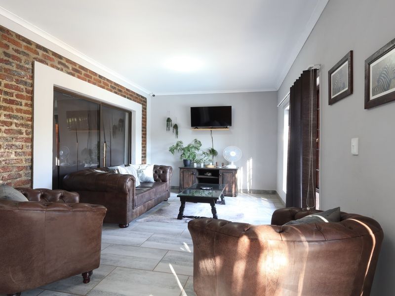A comfortable living room featuring an exposed brick accent wall, neutral tiled flooring, and large sliding glass doors providing natural light.