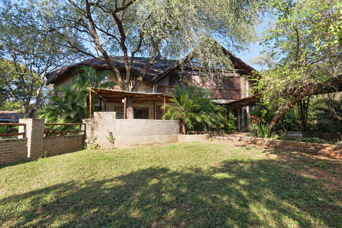 Rear view of a multi-story house featuring a thatched roof, brick boundary walls, and a timber pergola set within a mature garden.