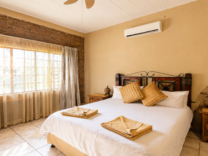 A bedroom featuring an exposed brick accent wall, tiled flooring, and a wall-mounted air conditioning unit.