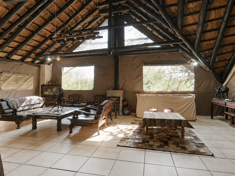 Spacious living area featuring a high vaulted thatched ceiling with exposed timber rafters, brick feature wall, and large canvas-style wall panels.