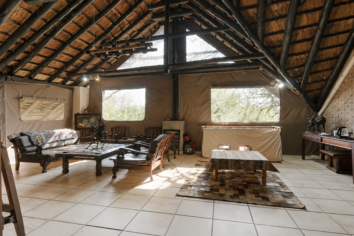 Spacious living area featuring a high vaulted thatched ceiling with exposed timber rafters, brick feature wall, and large canvas-style wall panels.