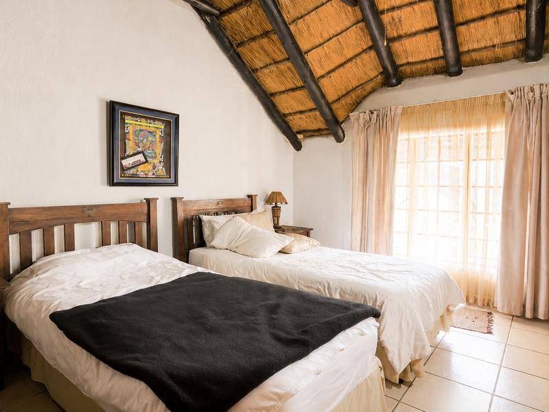A bedroom featuring a traditional thatched roof with exposed timber rafters, tiled flooring, and direct access to the outdoors via a sliding glass door.