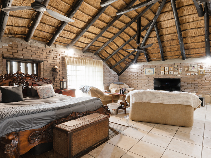 Spacious bedroom featuring a high vaulted thatched ceiling with exposed timber rafters, exposed brick walls, and tiled flooring.