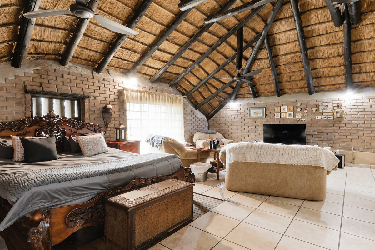 Spacious bedroom featuring a high vaulted thatched ceiling with exposed timber rafters, exposed brick walls, and tiled flooring.