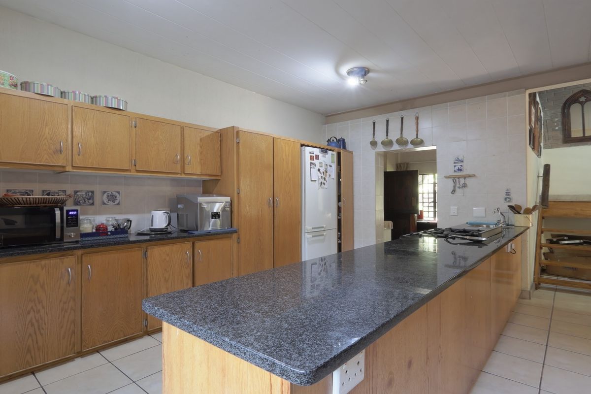 A functional kitchen featuring granite countertops, extensive wooden cabinetry, and a built-in gas hob, offering a practical layout with tiled flooring throughout.