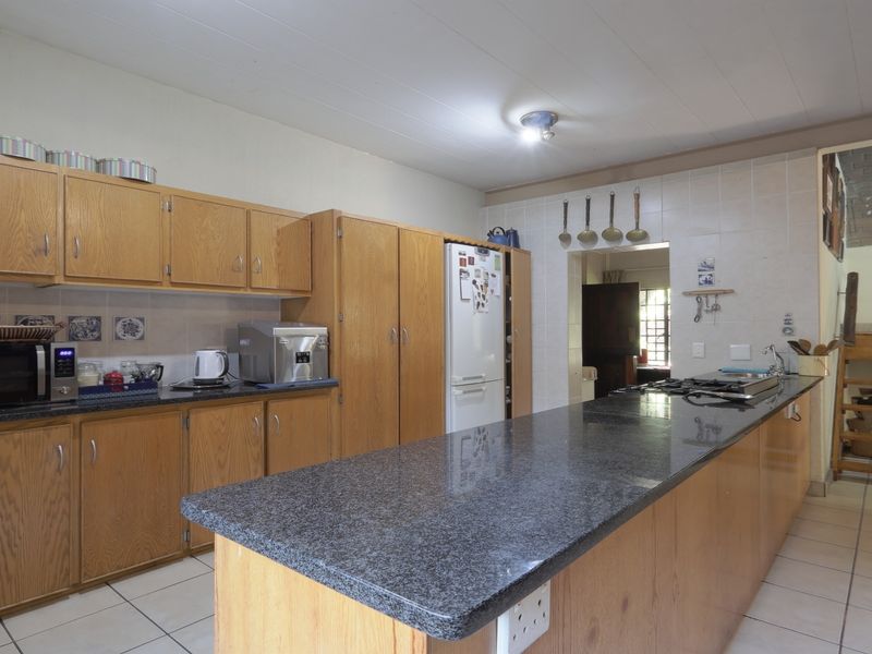 A functional kitchen featuring granite countertops, extensive wooden cabinetry, and a built-in gas hob, offering a practical layout with tiled flooring throughout.