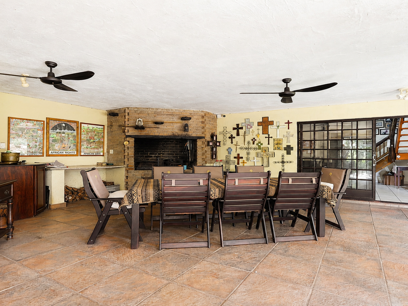Spacious covered patio featuring a large brick fireplace, tiled flooring, and dual ceiling fans, providing an ideal area for outdoor dining and entertaining.