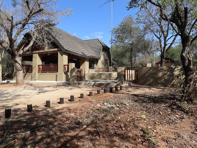 A well-maintained single-story residence featuring a tiled roof, covered patio with timber balustrades, and a surrounding masonry boundary wall in a natural setting.