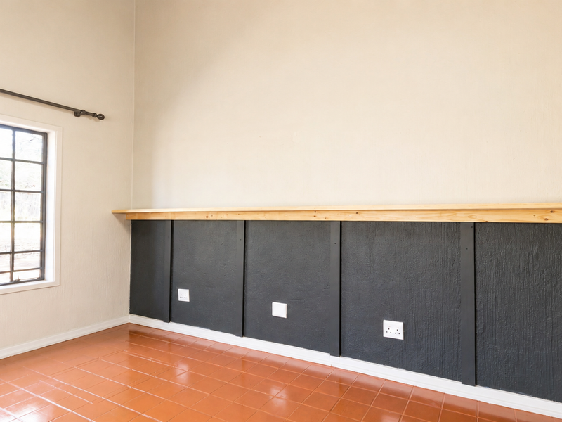 An empty living area featuring dark wainscoting with a wooden shelf, tiled flooring, and a steel-framed window.