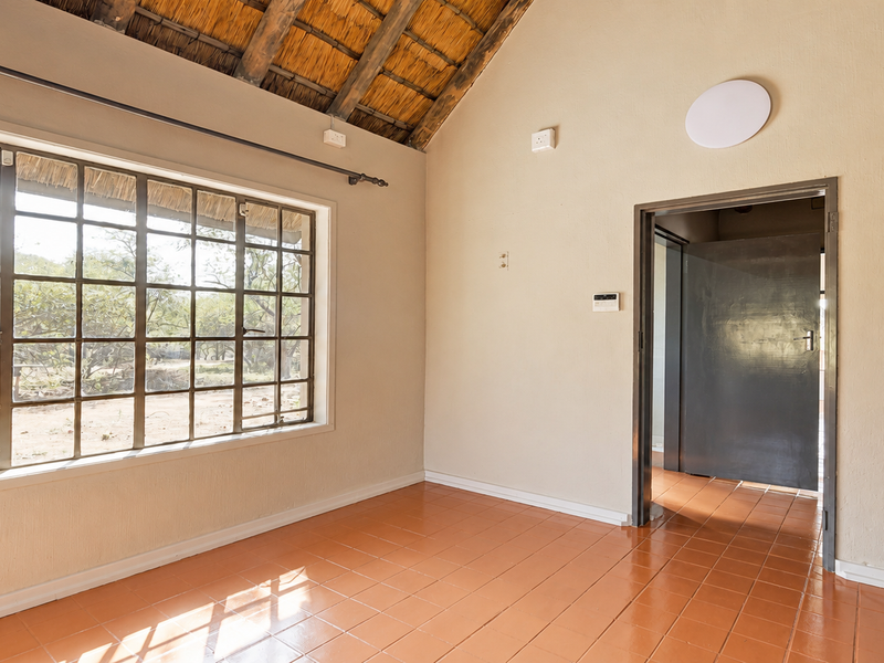An empty bedroom featuring a high thatched ceiling with exposed rafters, large steel-framed windows, and ceramic tile flooring.