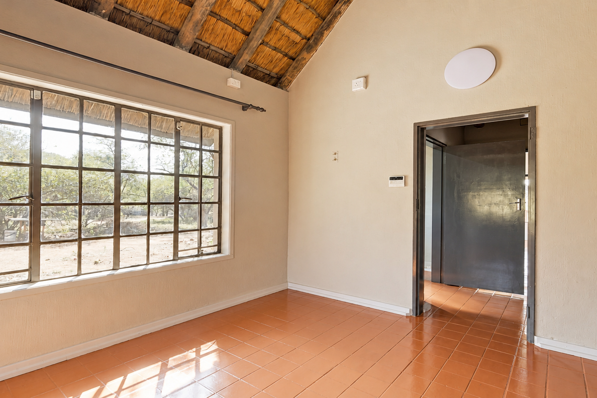An empty bedroom featuring a high thatched ceiling with exposed rafters, large steel-framed windows, and ceramic tile flooring.