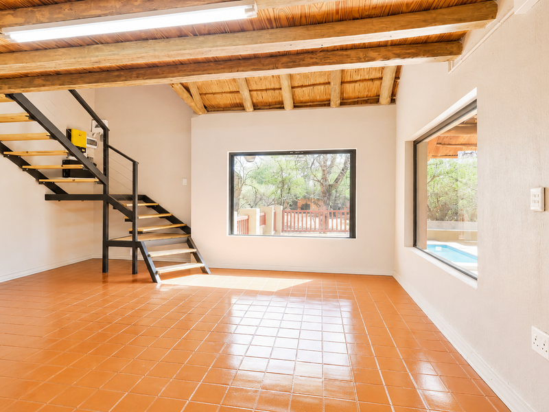 Spacious living area featuring exposed timber ceiling beams, tiled flooring, and a modern metal staircase with large windows overlooking the pool area.